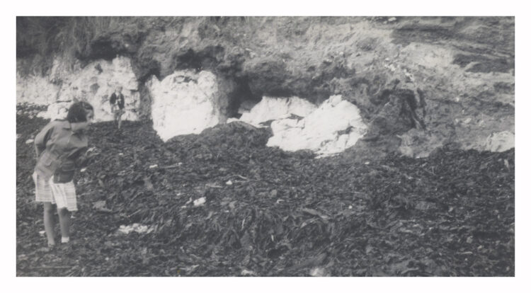 black and white photograph showing two small girls on a foreshore in front of low chalk cliff